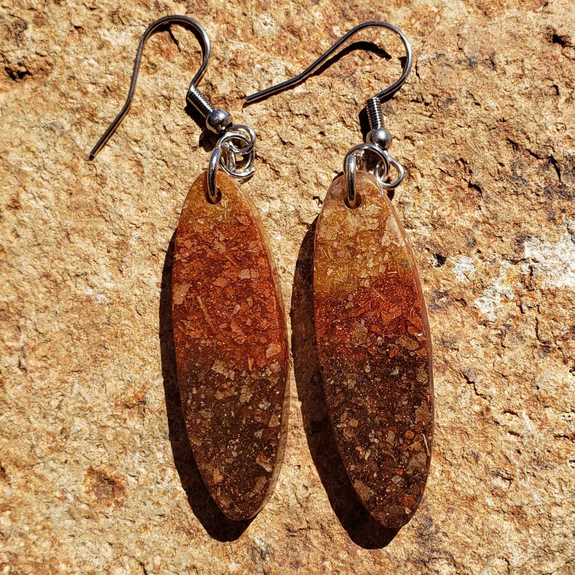 Pair of brown oval earrings made from dried leaves on a textured beige surface