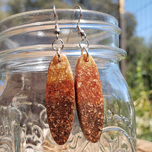 Brown textured earrings made from dried leaves hanging from a glass jar with a natural background