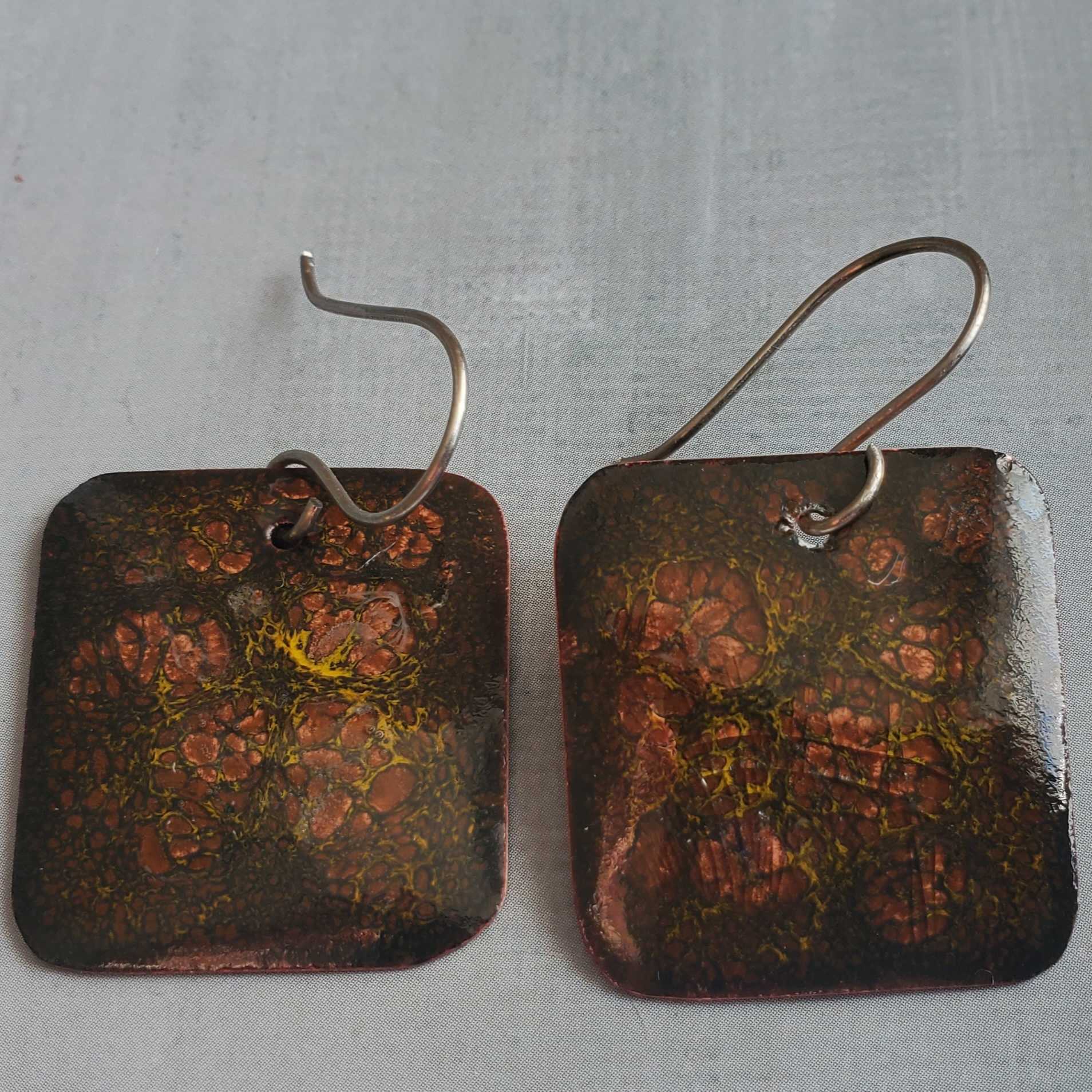Pair of square copper earrings with crackle pattern on a gray background