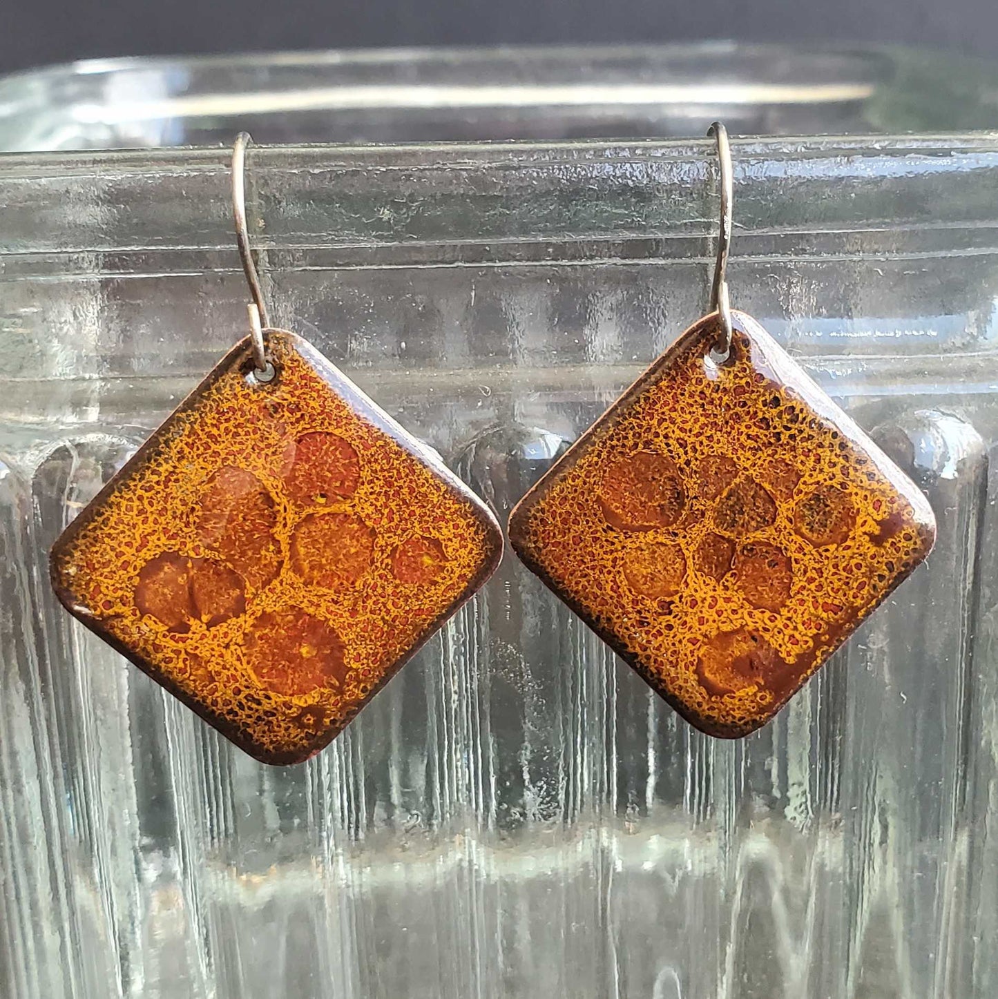 Square earrings with a textured brown surface on a clear glass background