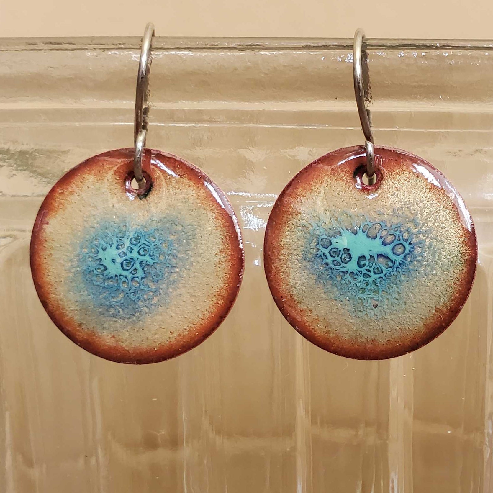 Round turquoise copper earrings with blue and brown design hanging from a glass jar.