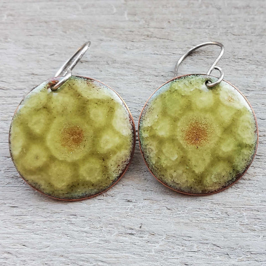 Pair of round green copper  earrings with a textured pattern on a light wooden surface