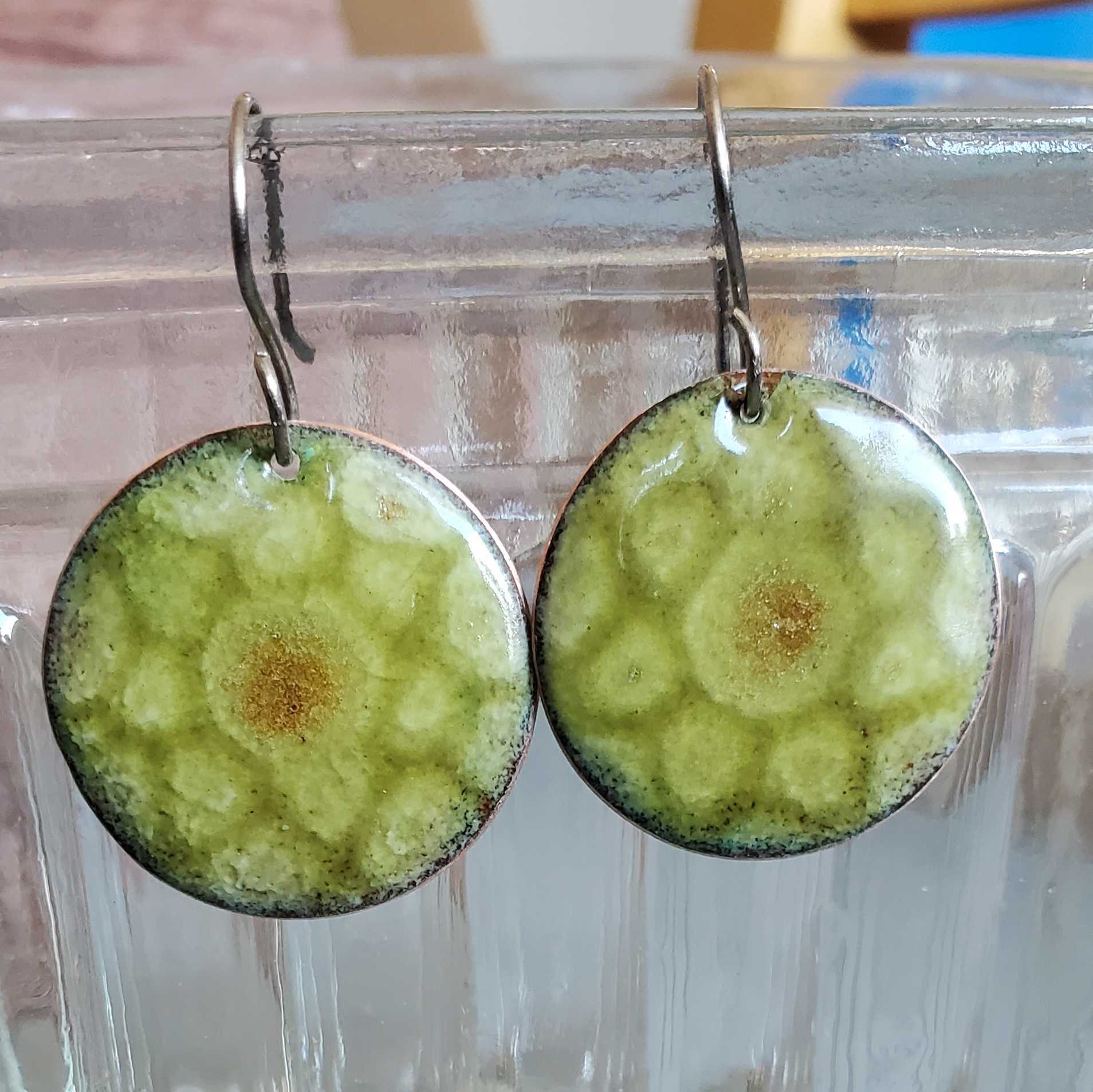 Green circular copper earrings with a brown center on a clear stand.