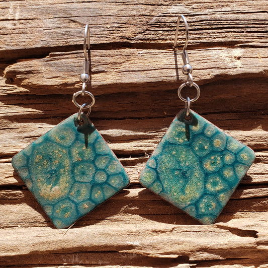 Pair of square copper enameled earrings, blue and yellow, on wooden surface