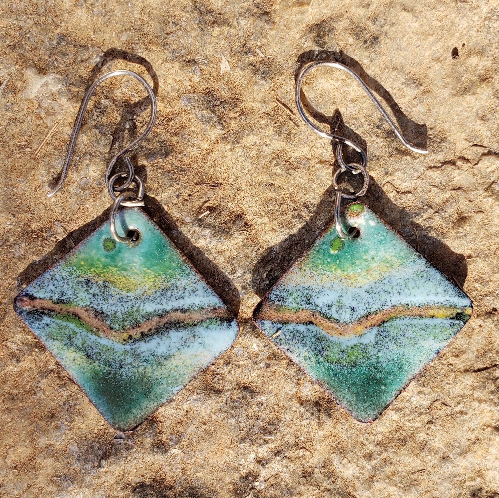 Pair of copper enamel earrings with green and brown colors on a textured stone background