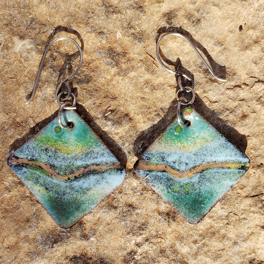 Pair of copper enamel earrings with green and brown colors on a textured stone background