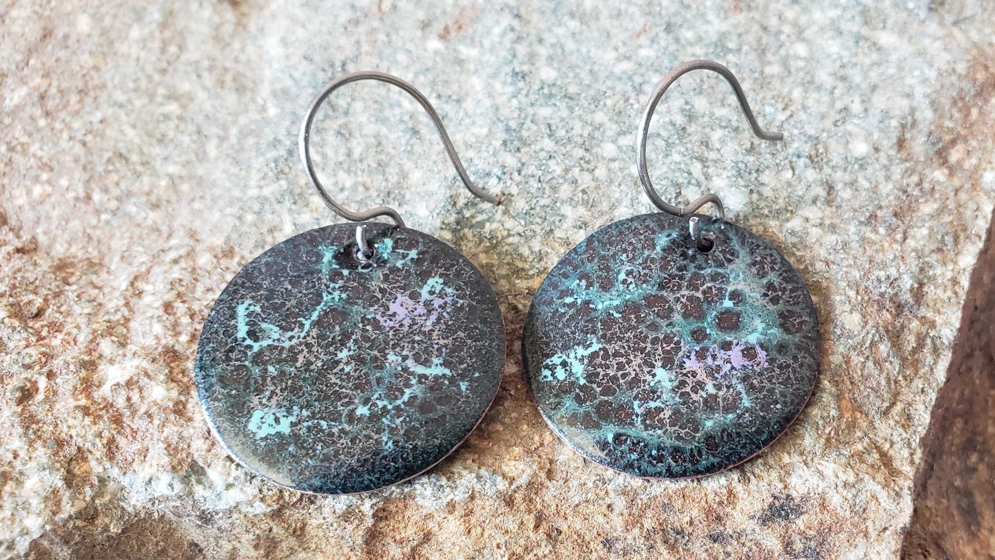 Pair of round copper earrings with a textured surface on a stone background