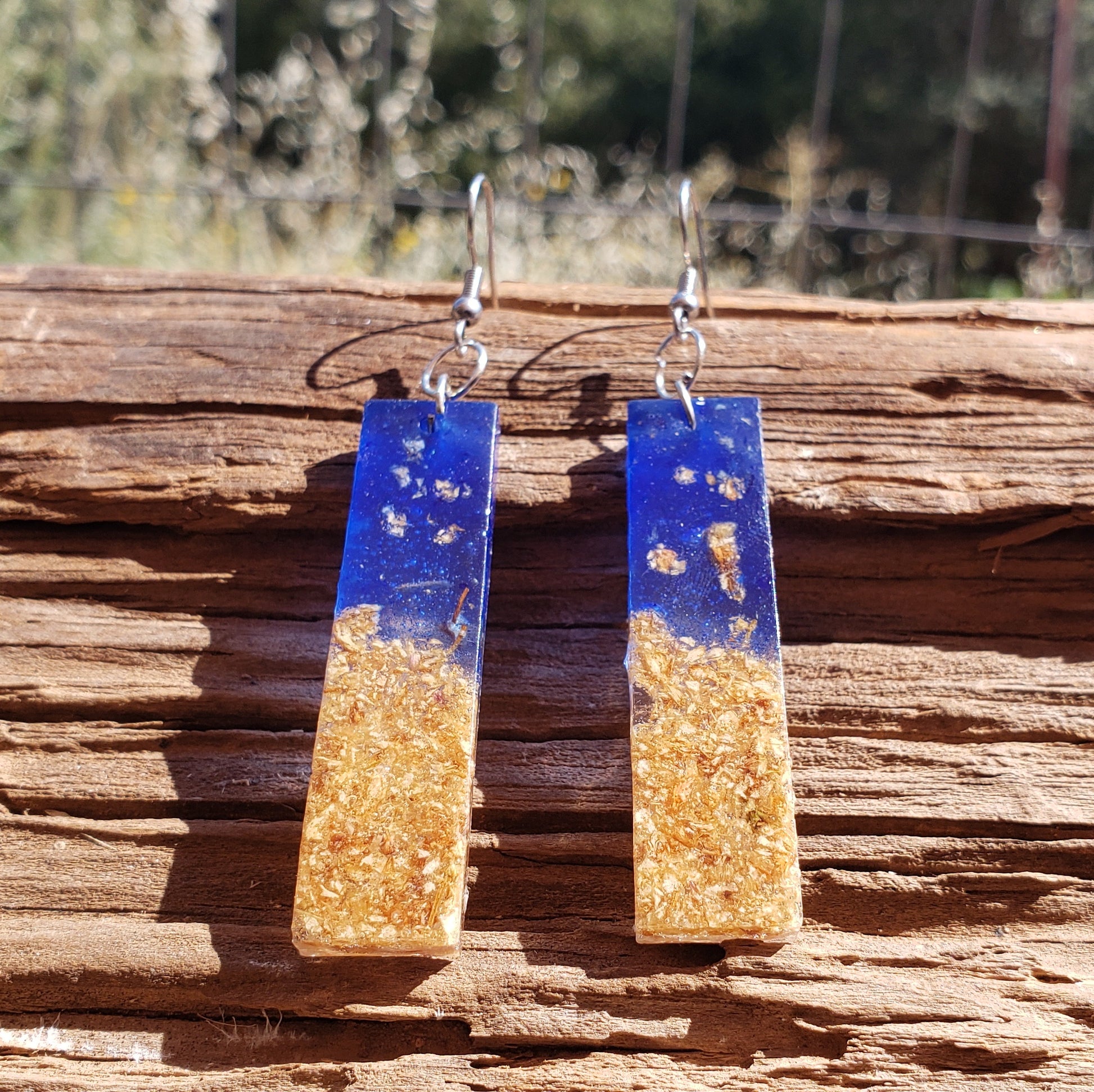 Pair of blue and gold earrings with dried flowers on a wooden surface