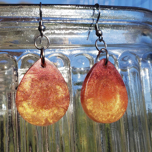 Teardrop-shaped fire flame colored earrings with a metallic finish on a reflective surface
