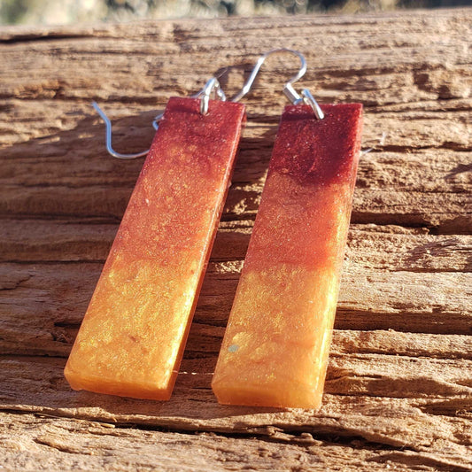 Pair of flame fire colored rectangular earrings with a gradient from red to orange on a wooden surface.
