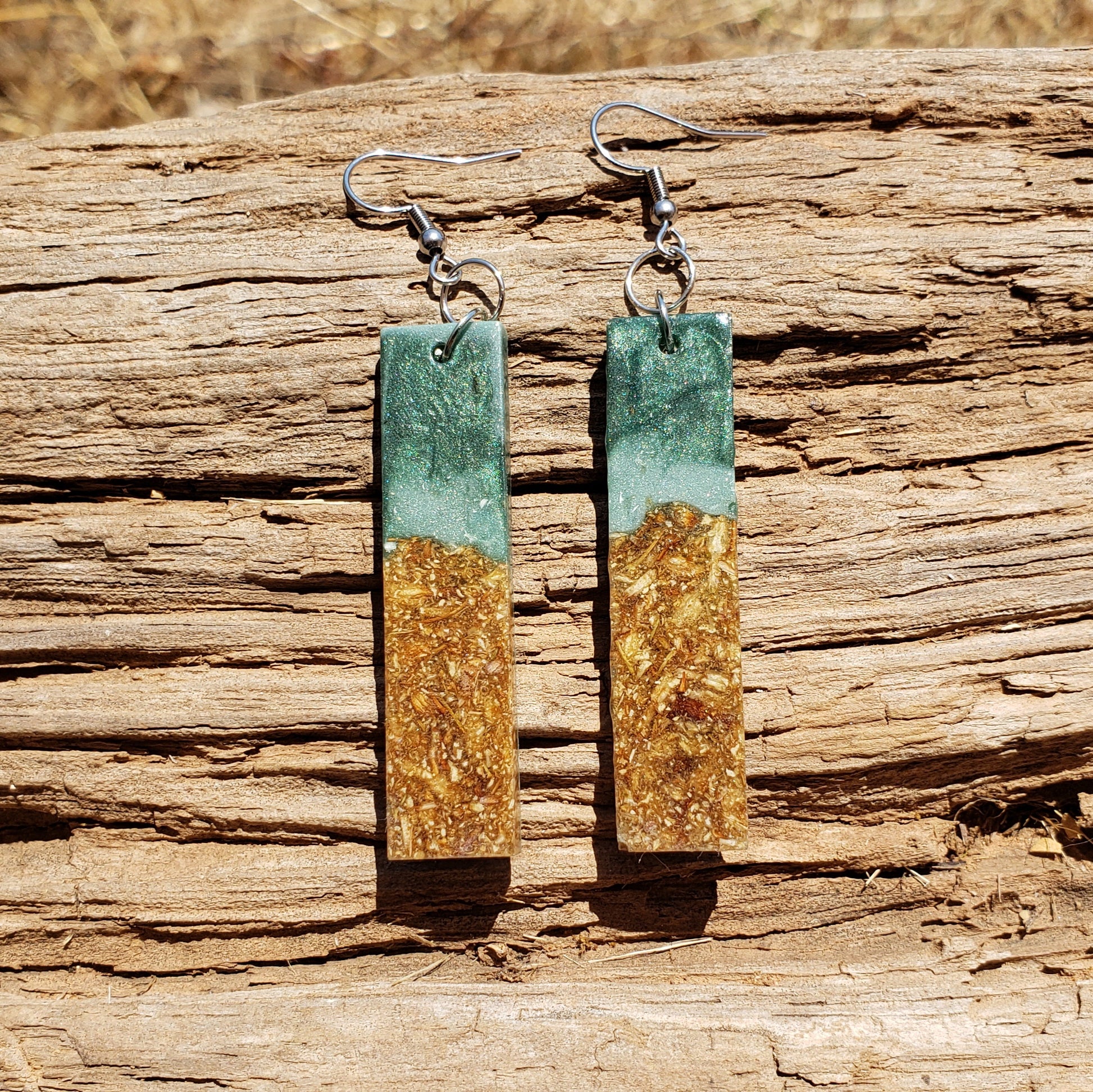 Pair of earrings with green and gold design on a wooden surface