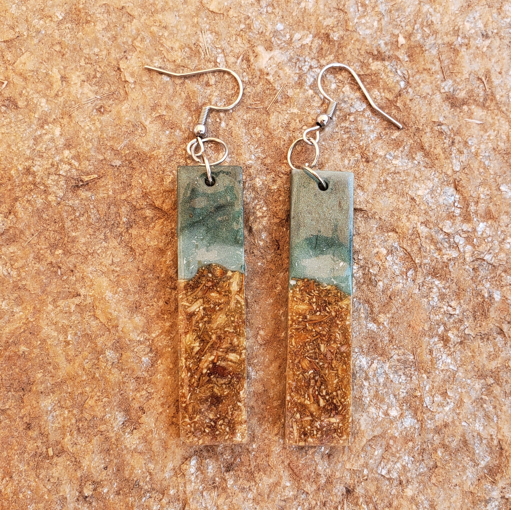 Pair of earrings with rectangular green and gold design on a textured brown surface