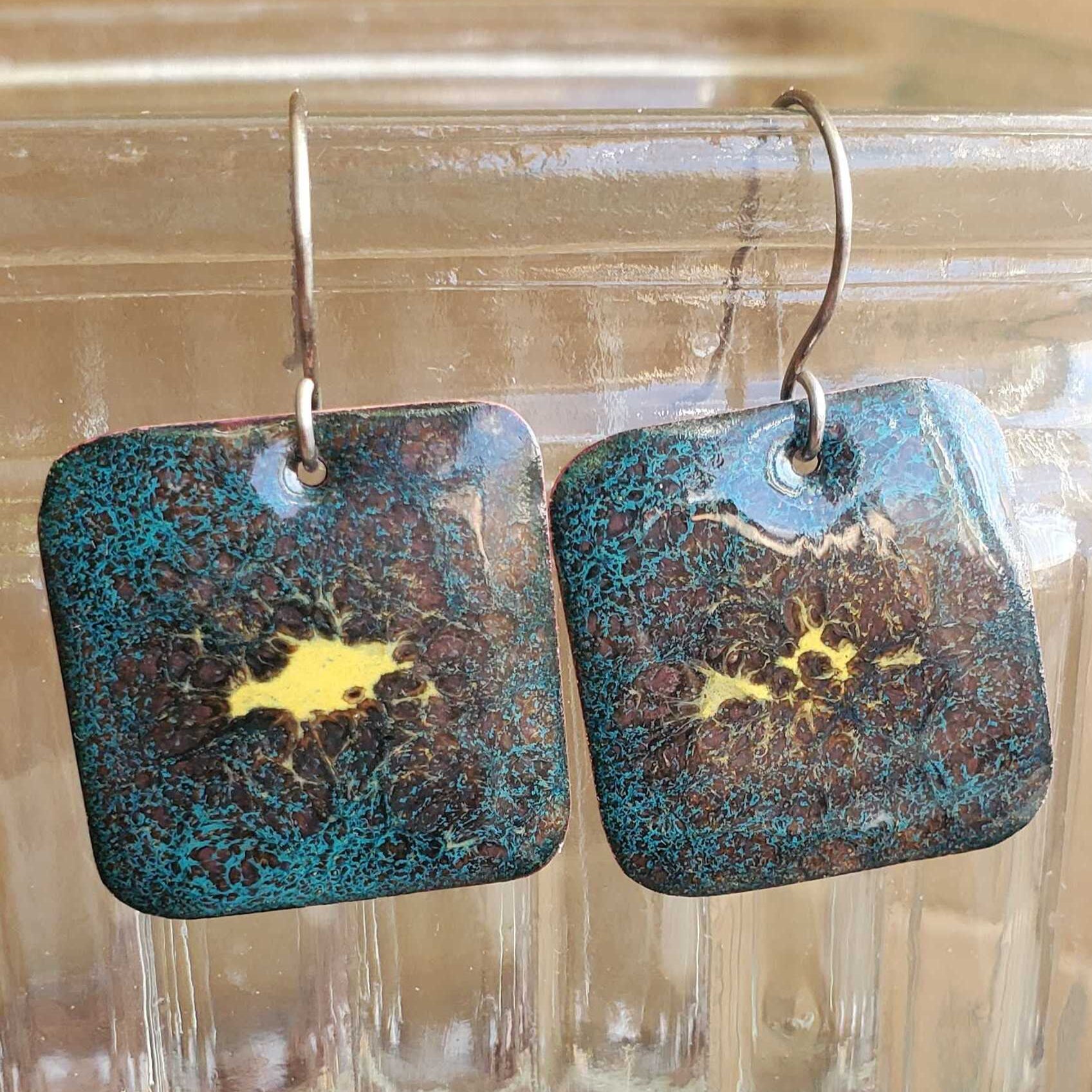 Pair of copper enamel earrings with blue and gold design on a glass surface