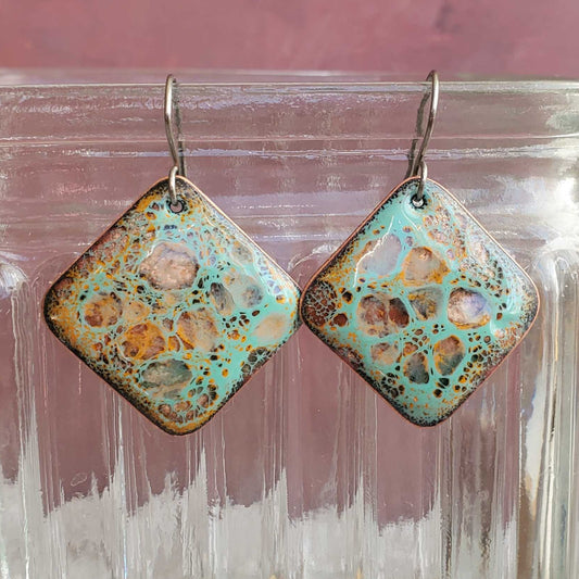 Square-shaped earrings with a decorative pattern on a glass jar.