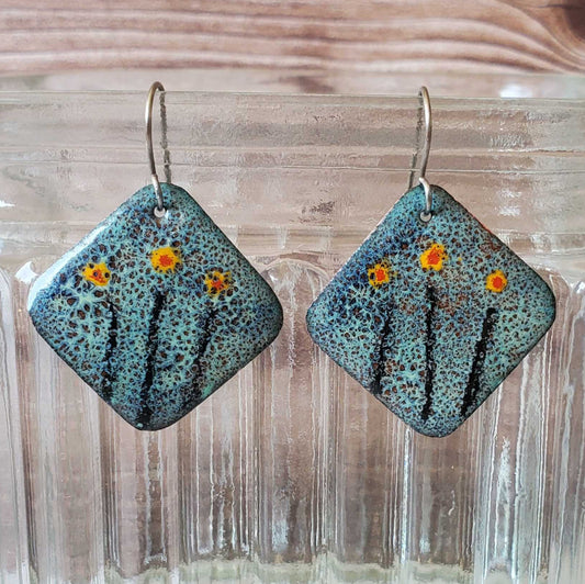 Square copper earrings with floral design on a wooden surface