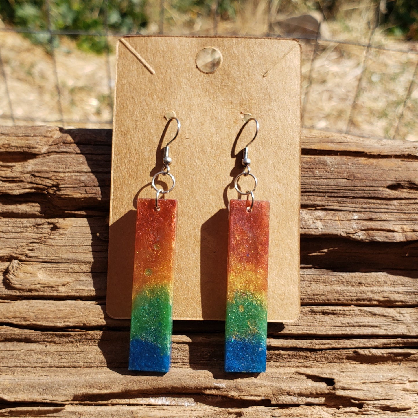 Colorful bar-shaped rainbow earrings on a wooden stand with a natural background
