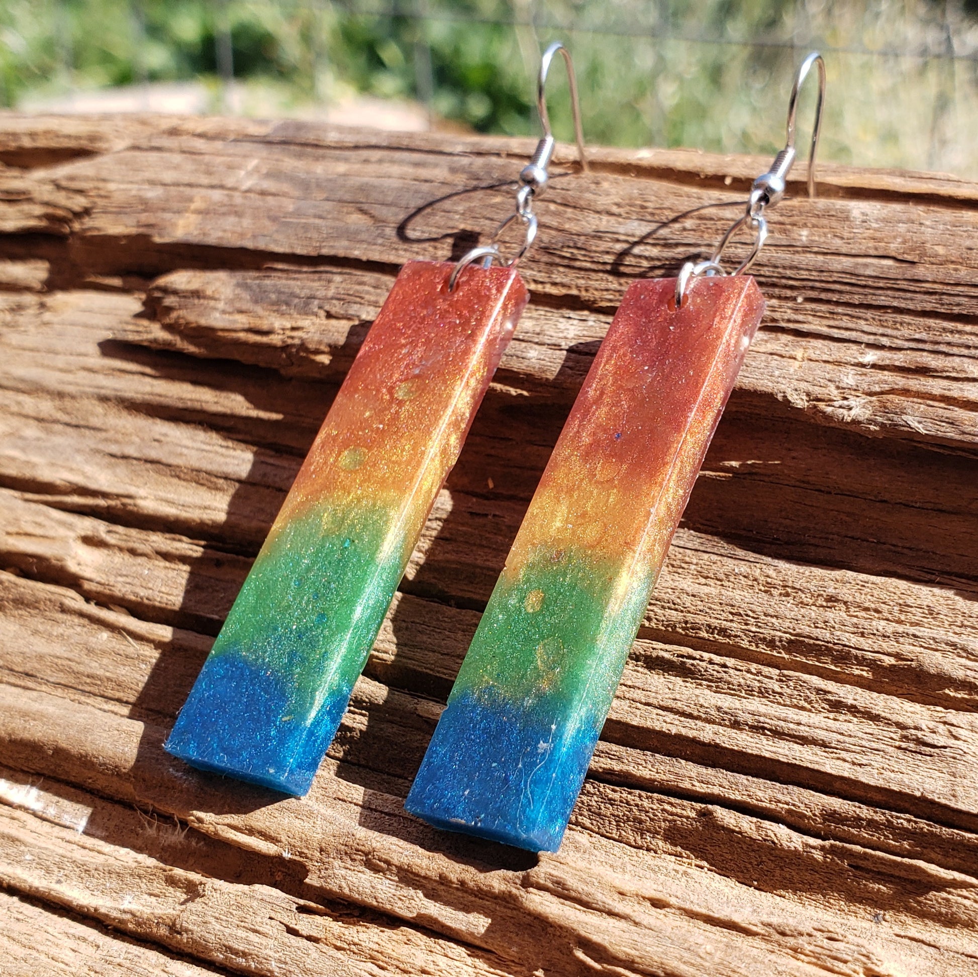 Colorful rectangular rainbow earrings on a wooden surface
